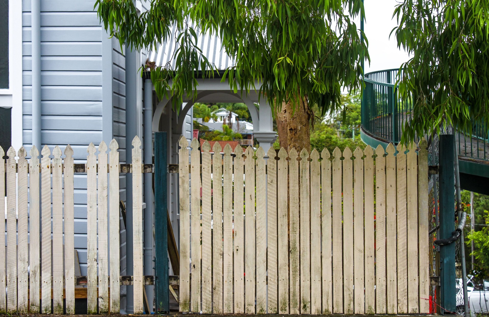 Common neighborhood scene in Brisbane Australia - old picket fence next to houses and tropical vegetation